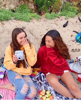 picture of my friend and I laughing on the beach with our polaroid camera and snacks